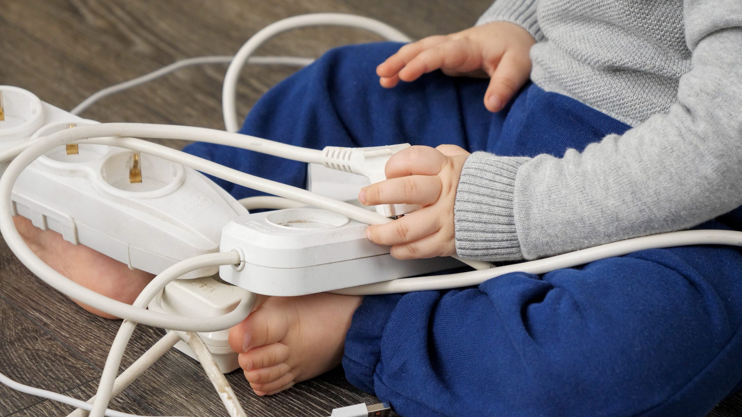 Closeup of little baby boy inserting electric plug. CHild playing with wires and cables